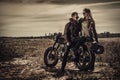 Young, stylish cafe racer couple on vintage custom motorcycles in field