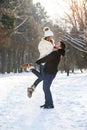 Young stylish couple in love have fun while walking on the snowy winter park. Handsome young man holds his beautiful Royalty Free Stock Photo
