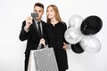 Young stylish couple, a man in a suit and a girl in a black dress holding balloons and bags, shopping, a man holding a credit car Royalty Free Stock Photo