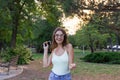 Young stylish cute girl is listening to music in headphones on mobile phone and dancing in the park. Pretty woman is relaxing and Royalty Free Stock Photo