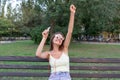 Young stylish cute girl is listening to music in headphones on mobile phone and dancing in the park. Pretty woman is relaxing and Royalty Free Stock Photo