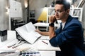Young stylish dark-haired architect in glasses and in a blue jacket is working with documents on the desk in the office Royalty Free Stock Photo