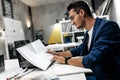 Young stylish dark-haired architect in glasses and in a blue jacket is working with documents on the desk in the office Royalty Free Stock Photo