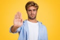 Young stylish European man makes stop gesture on yellow background