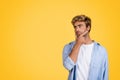 Young stylish European man thinking, hand on chin, yellow studio background