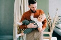 A young stylish father in trend orange shirt plays with his young son in a brown hat in his arms in a spacious stylish Royalty Free Stock Photo