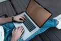 Young stylish freelancer man in blue jeans in sneakers is typing on a metallic modern laptop indoors. Guy works