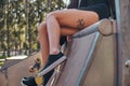 Girl`s legs with a tattoo. Young stylish girl sitting on a ramp in the skate park at the summertime. Royalty Free Stock Photo