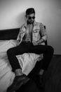 Young stylish guy in denim jacket on the bed. black and white photo with fine grain effect. selective focus Royalty Free Stock Photo