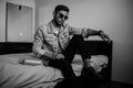 A young stylish guy in a denim jacket on the bed with a bottle of alcohol. black and white photo with fine grain effect. selective Royalty Free Stock Photo