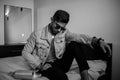 A young stylish guy in a denim jacket on the bed with a bottle of alcohol. black and white photo with fine grain effect. selective Royalty Free Stock Photo