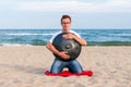 Young stylish guy sitting on the sand beach and holding a handpan or hang with sea On Background. The Hang is