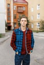 Young stylish handsome man in a red fashionable t-shirt in a blue and red plaid shirt walks through a small town