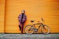 Young stylish hipster man standing with a cruiser city Bicycle near orange Wall. Student Resting after ride bicycle. Eco