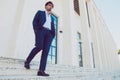 Young stylish man with hands in pockets walking down the stairs outside a white building