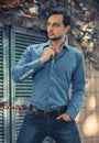 Young stylish man model in jeans and shirt posing in modern park architecture place. Fashion shot. Royalty Free Stock Photo