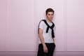 Young stylish man model in a vintage white t-shirt with a shirt with a hairstyle in black jeans stands near a modern pink wall Royalty Free Stock Photo