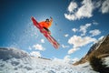 A young stylish man in sunglasses and a cap performs a trick in jumping with a kicker of snow against the blue sky and Royalty Free Stock Photo