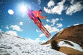 A young stylish man in sunglasses and a cap performs a trick in jumping with a kicker of snow against the blue sky and Royalty Free Stock Photo