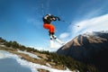 A young stylish man in sunglasses and a cap performs a trick in jumping with a kicker of snow against the blue sky and Royalty Free Stock Photo