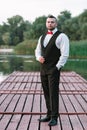 Young stylish man in a waistcoat, vertical portrait of the groom, portrait on a background of nature, the river and the pier