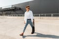 Young stylish young man walks on the street on a sunny day. Urban hipster guy in fashionable clothes in summer shoes with a bag in Royalty Free Stock Photo