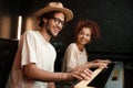 Young stylish musicians happily playing on piano keyboard recording song in modern recording studio