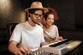 Young stylish musicians happily recording song on piano keyboard in modern sound studio. Attractive creative man and