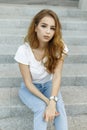 Young stylish pretty woman in trendy vintage jeans in a white stylish t-shirt is resting sitting on the steps.