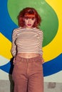 Young stylish redhead Caucasian woman in retro style of 70s posing at wall looking into camera Royalty Free Stock Photo