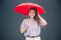 Young stylish trendy woman isolated over grey blue background. Beautiful cheerful girl stand under red umbrella for rain Royalty Free Stock Photo