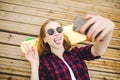 Young stylish urban girl in hipster outfit making selfie while lying with on wooden pier Royalty Free Stock Photo