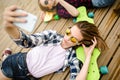 Young stylish urban girl in hipster outfit making selfie while lying with on wooden pier Royalty Free Stock Photo