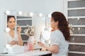 Young stylish woman applying makeup by eye shadow brush in mirror