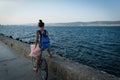 Young stylish woman in dress and with backpack is riding bicycle on promenade Royalty Free Stock Photo