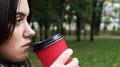 Young stylish woman drinks morning hot coffee in red eco paper cup outdoors in autumn park. Close-up side view of young woman Royalty Free Stock Photo