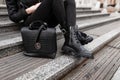 Young stylish woman in fashionable autumn black clothes sits on the steps in the city. Close-up of female legs in jeans in boots