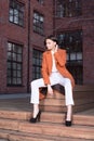 Young stylish woman in a red coat and white pants sitting on the wooden stairs Royalty Free Stock Photo