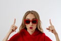 Young stylish woman with red lips, sunglasses and sweatshirt poiting copy space isolated on white background. Closeup girl face Royalty Free Stock Photo