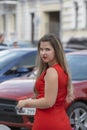 Young stylish woman wearing red dress and red lipstick walking on the city street near cars. Plus size model Royalty Free Stock Photo