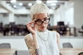 Young and succesful. Portrait of confident blonde tattooed businesswoman adjusting her eyeglasses and looking at camera Royalty Free Stock Photo
