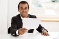 Young successful african businessman smiling, holding paper, sitting at workplace. Royalty Free Stock Photo