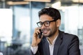 Young successful arab businessman boss talking on phone close up, man smiling contentedly inside office at workplace in Royalty Free Stock Photo