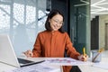 Young successful asian financier working inside office with papers, businesswoman behind paperwork joyfully recording