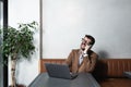 Young successful businessman sitting in cafeteria drinking coffee and is happy looking stock market prices going up. Male getting