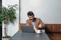 Young successful businessman sitting in cafeteria drinking coffee and is happy looking stock market prices going up. Male getting