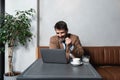 Young successful businessman sitting in cafeteria drinking coffee and is happy looking stock market prices going up. Male getting