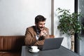 Young successful businessman sitting in cafeteria drinking coffee and is happy looking stock market prices going up. Male getting