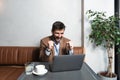 Young successful businessman sitting in cafeteria drinking coffee and is happy looking stock market prices going up. Male getting