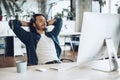 Young businessman sitting in office with hands behind his head satisfied with work done